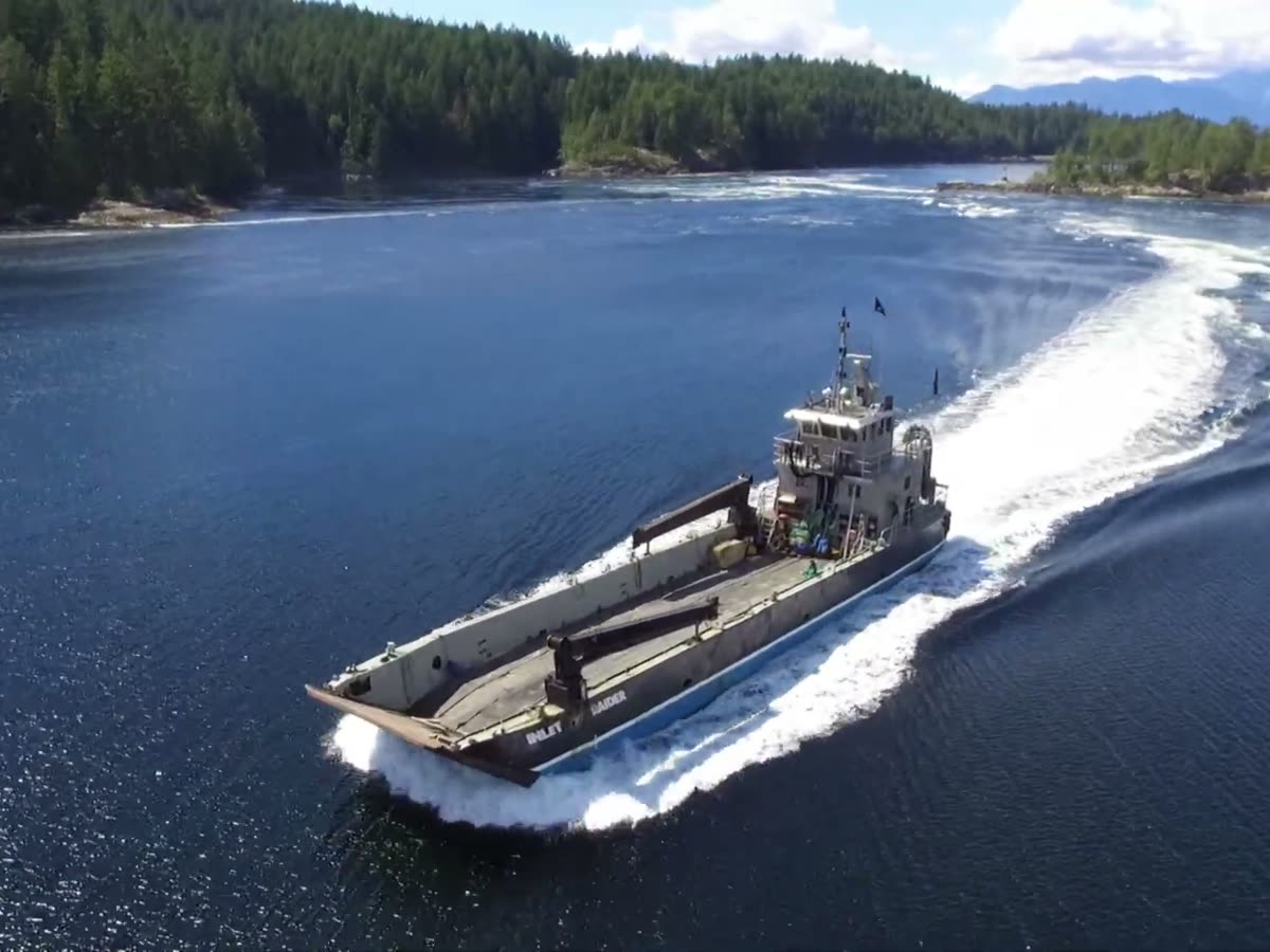 Aerial of the Inlet Raider underway with a long curving wake, wooded islands behind