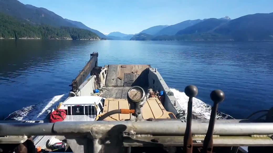 A white pickup on deck, running up a calm inlet between mountains